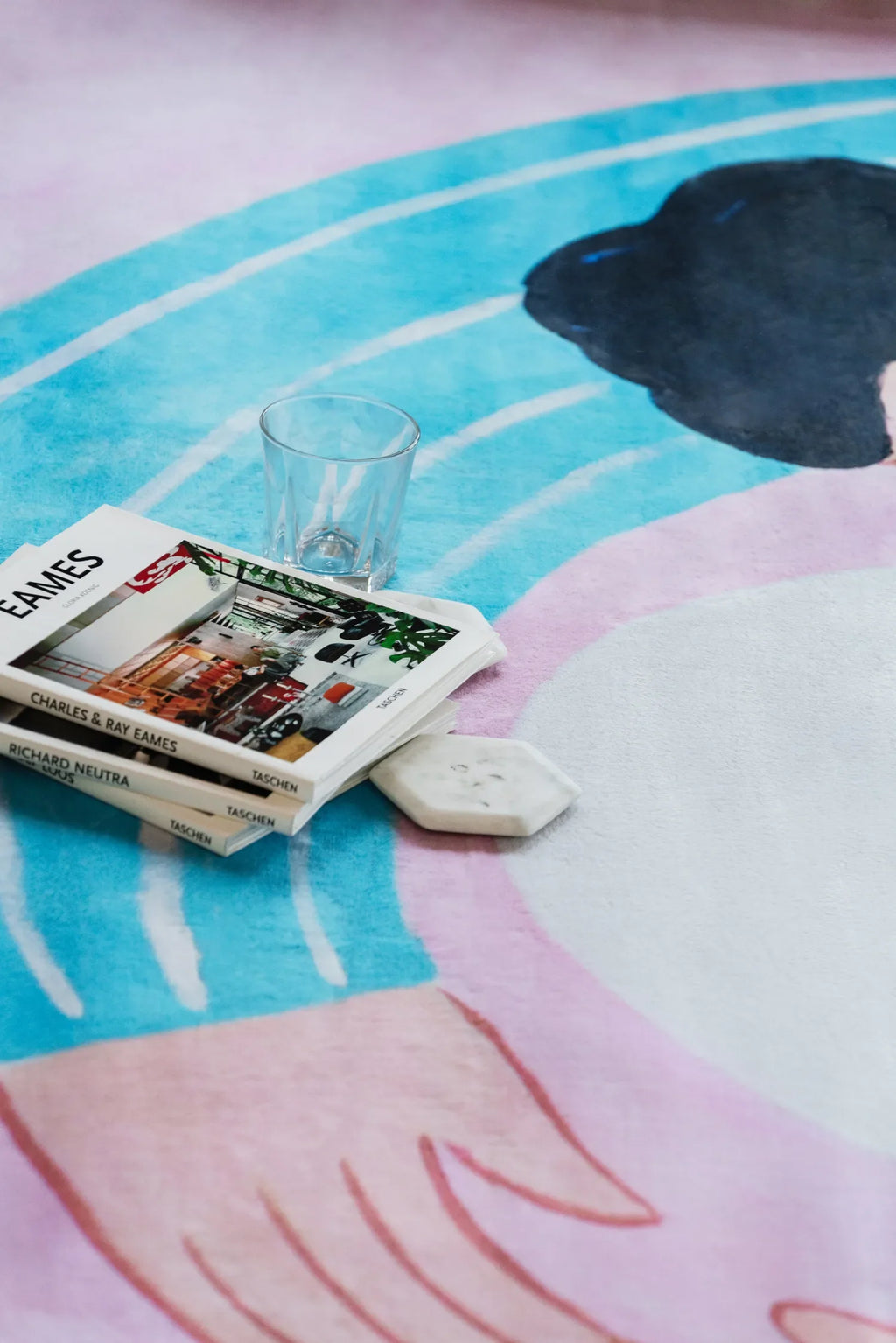 A cat lover rug in lilac and blue, styled with books and a clear glass resting casually on its illustrated surface.