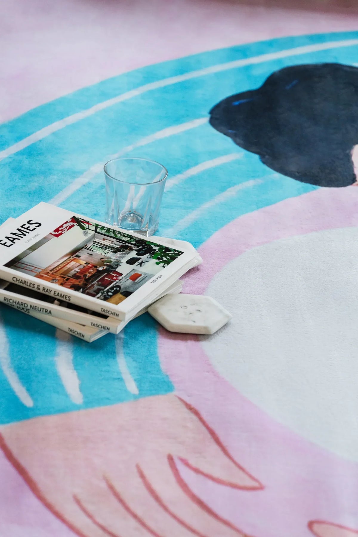 A cat lover rug in lilac and blue, styled with books and a clear glass resting casually on its illustrated surface.