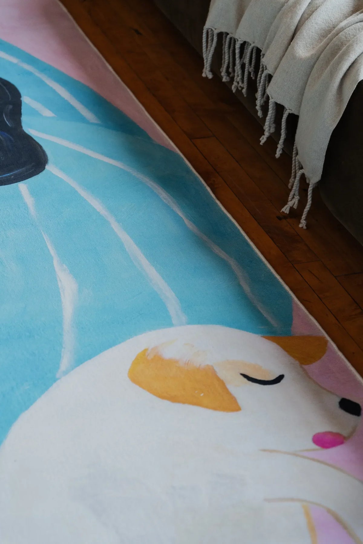 Artistic cat lover rug in lilac and blue, highlighting the sleeping cat detail beside a soft gray throw on the wooden floor.