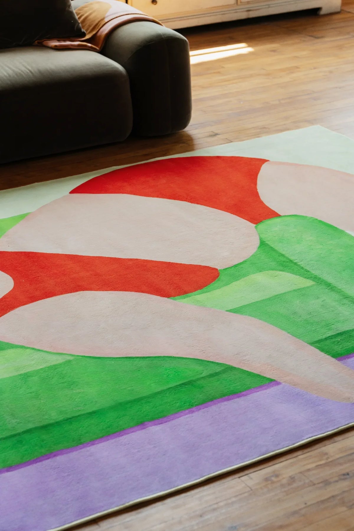 Modern Abstract Body Art Rug by Nimei with bold red and green shapes, styled beside a dark sofa on polished wooden floor.