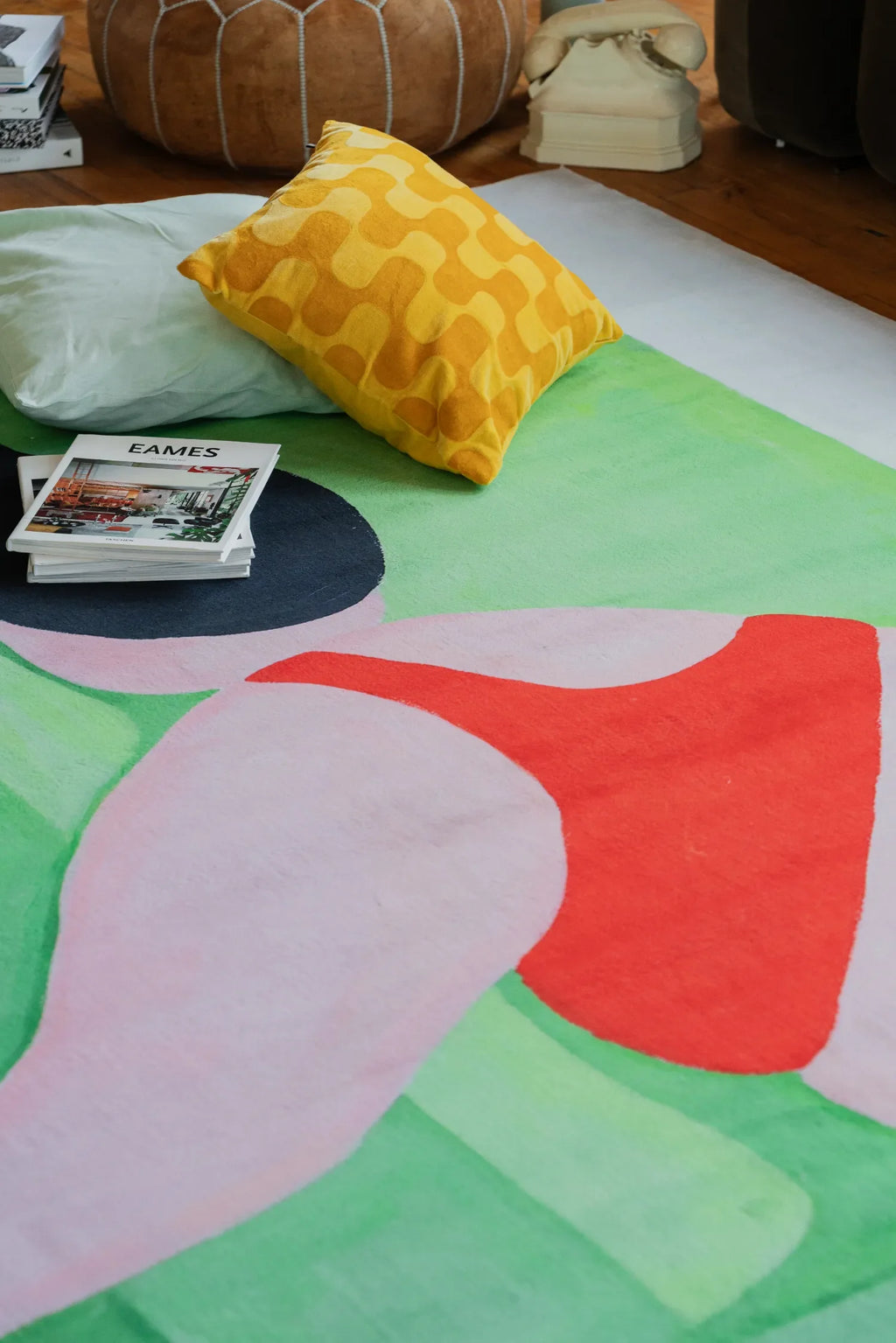 Close-up of abstract body art rug showing vibrant red and pink curves against fresh green blocks, paired with yellow cushion and pouf.