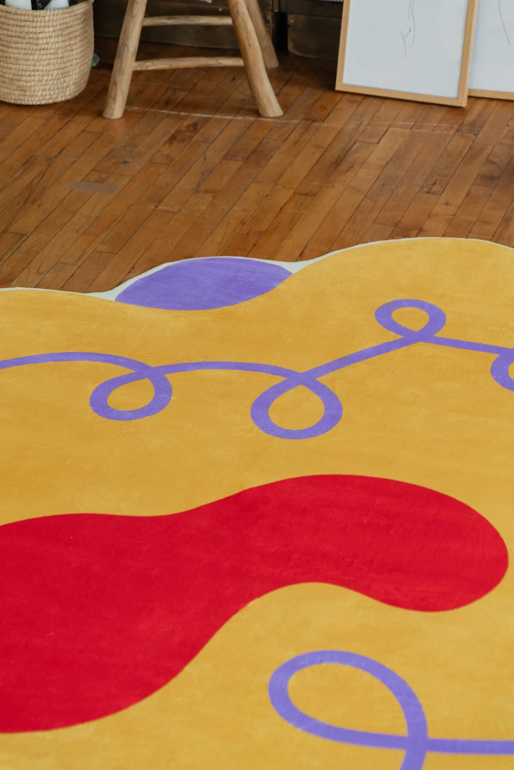 Yellow Abstract Funky Rug with bold red accents, styled near a woven basket and wooden stool on hardwood floor.