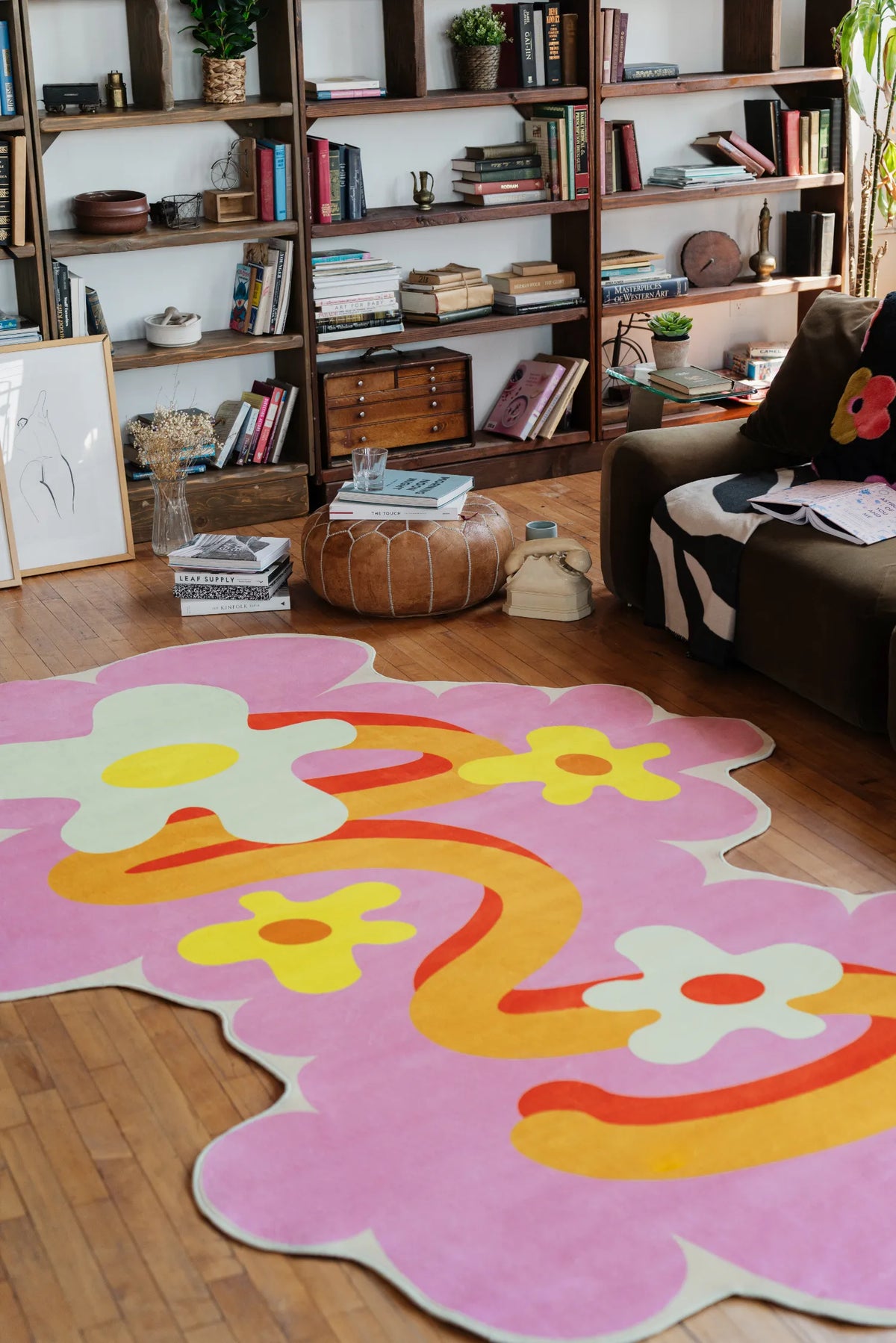Close view of an irregular rug in pink floral design placed on wood floor beside a cushioned sofa and open shelving unit.