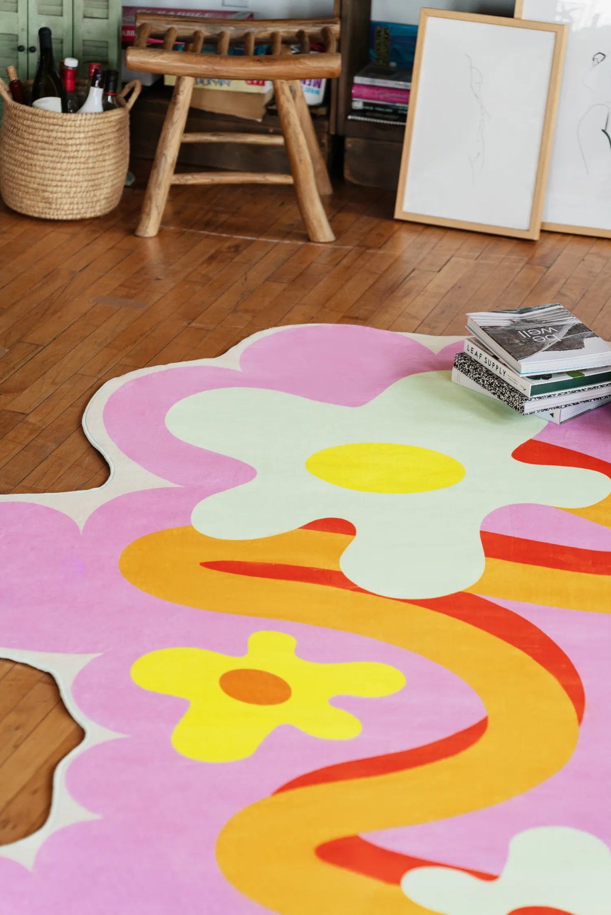 An irregular-shapd rug with bright floral waves placed in a cozy corner on wood floor near open shelving and a wooden chair.