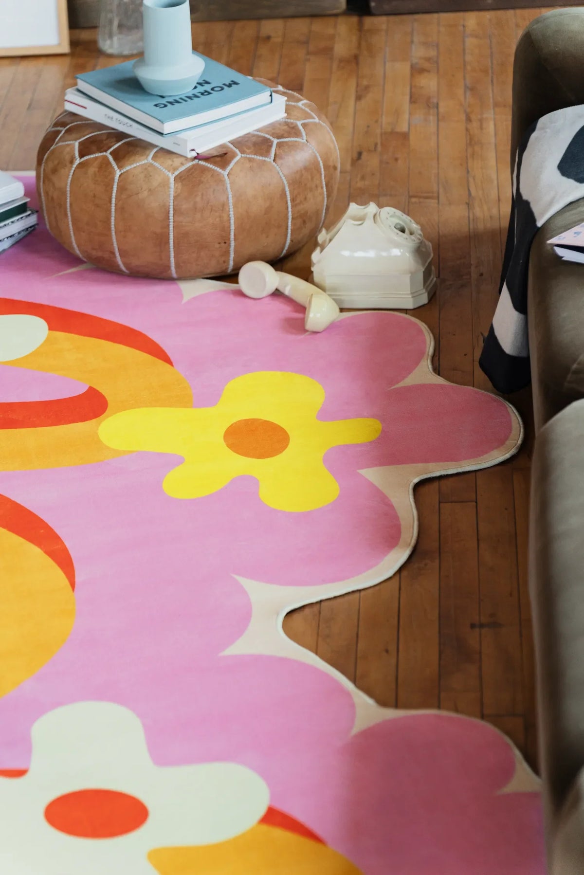 Playful rug with pink floral design resting on wood floor beside a deep sofa and a round leather ottoman.