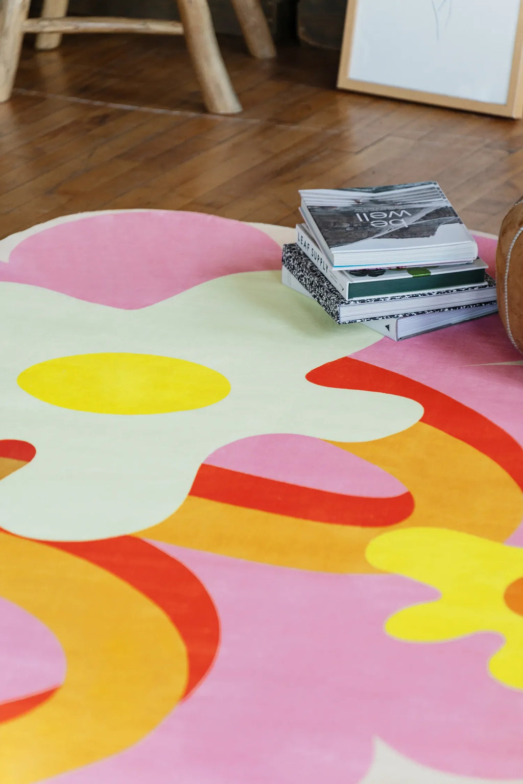 Close view of a playful rug with bold floral shapes on wood floor beside a low stool and stacked books.
