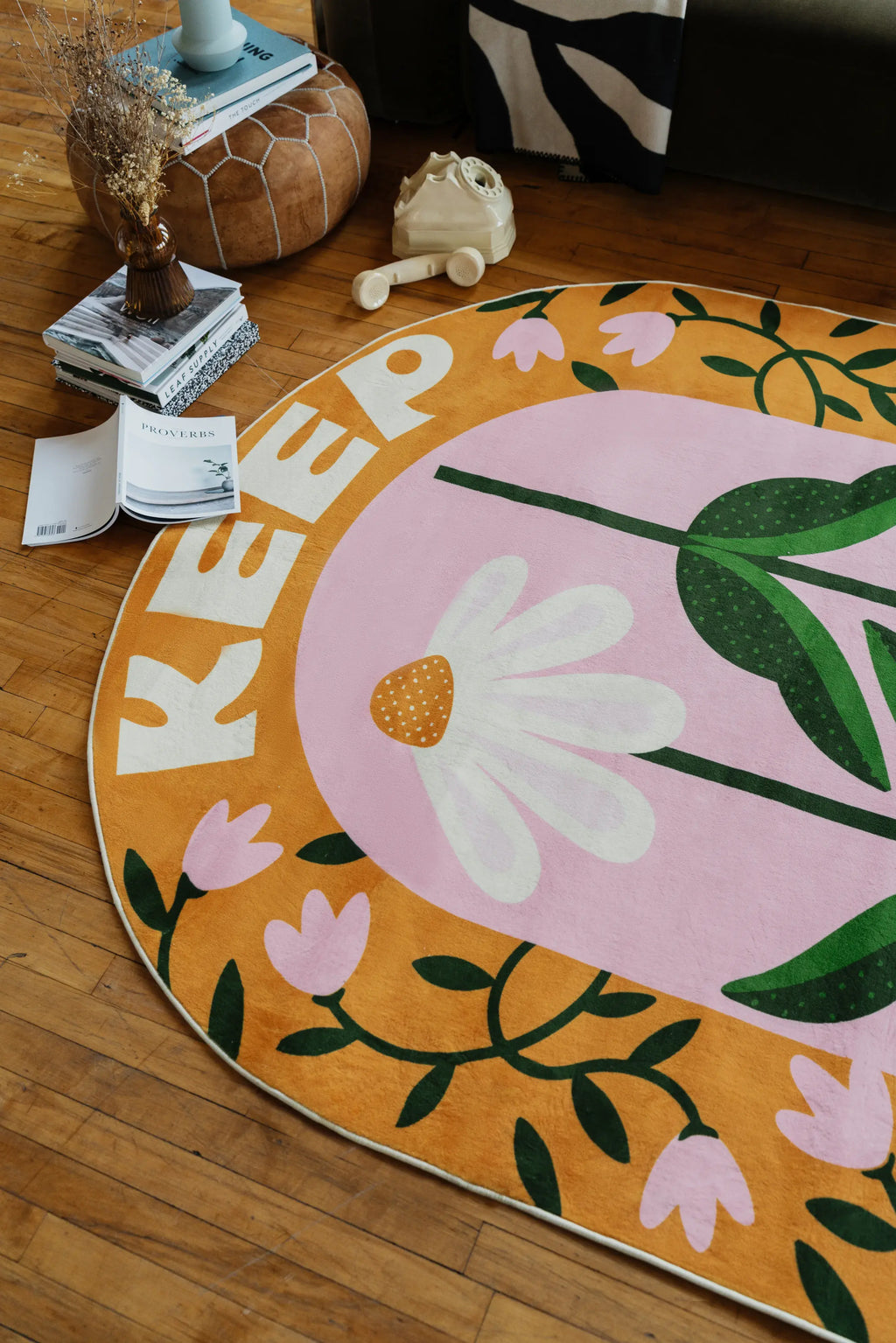 Playful rug in oval daisy design spread across warm wood floor near sofa and pouf with vintage rotary phone in cozy living room