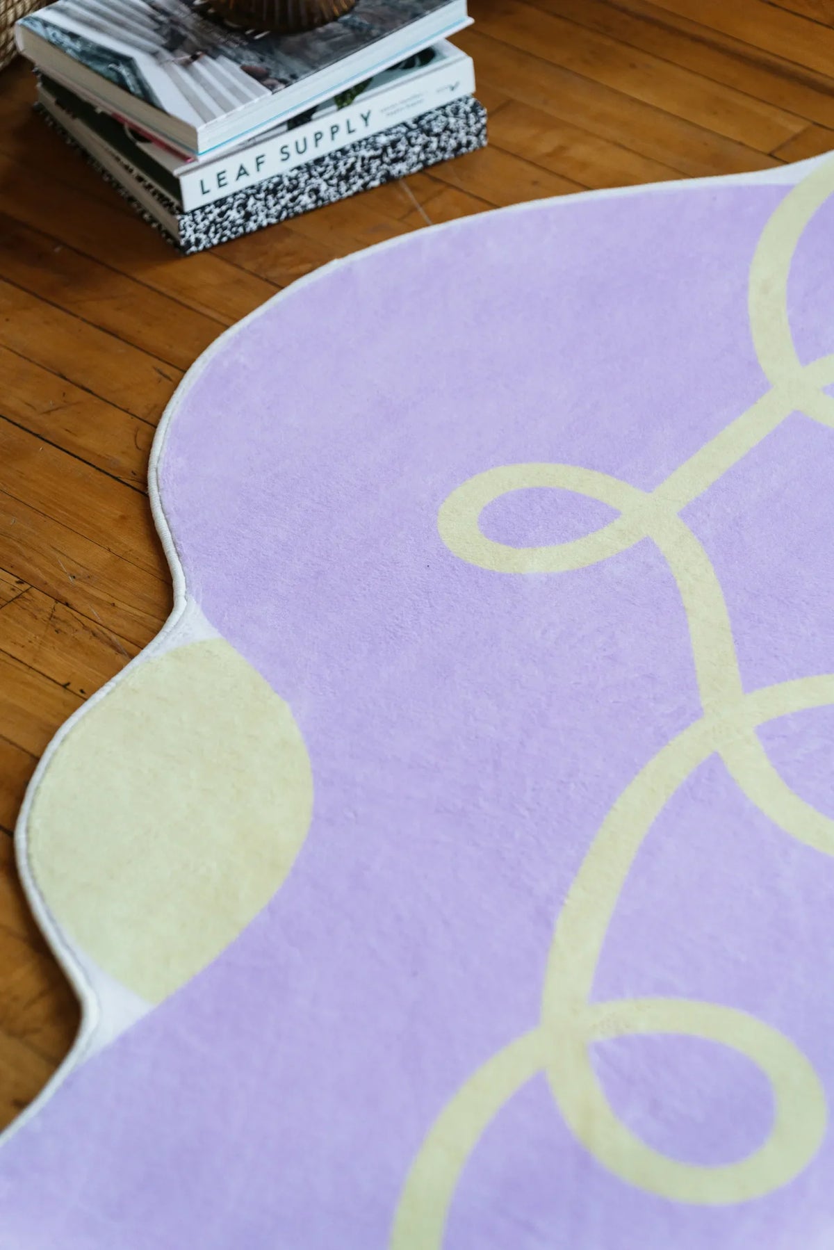 Detail of lilac funky rug showing cream patches and yellow swirl patterns, adding charm to a cozy living room with wooden floor.