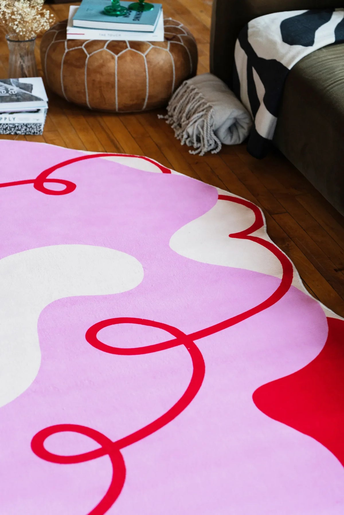 Funky pink rug in 5'X7' size with red flowing lines, placed by a sofa and pouf with books in a cozy living room.