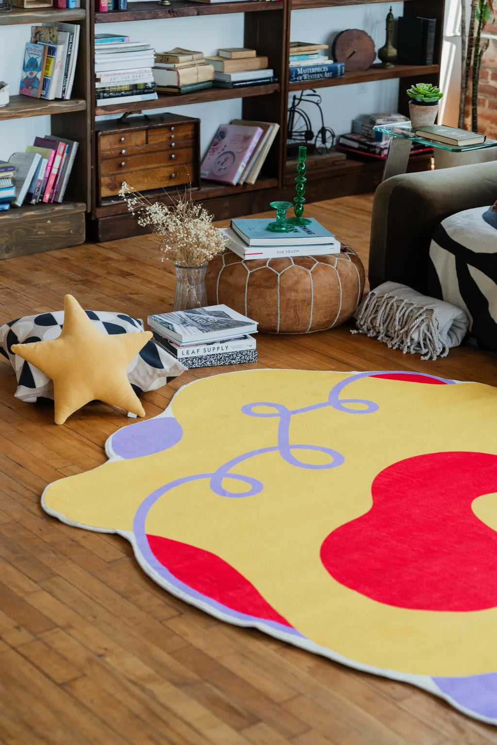 Yellow wavy abstract rug adds a playful pop of color beside a round pouf and star pillow in a warm living space.