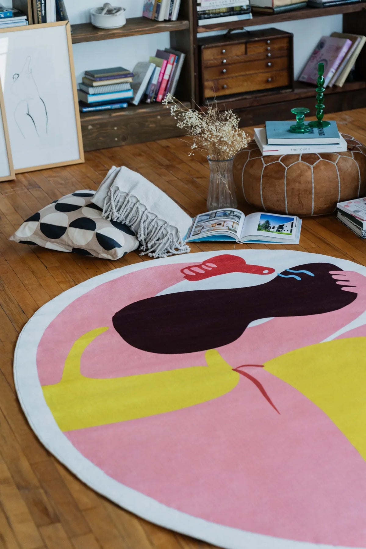Funky body art rug angled beside a pouf and stacked books, bright colors adding a playful note to the living space.