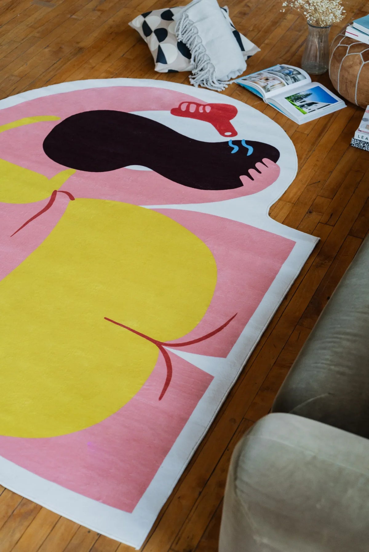 Round funky rug with bold yellow and pink blocks, viewed from sofa side with scattered books nearby.