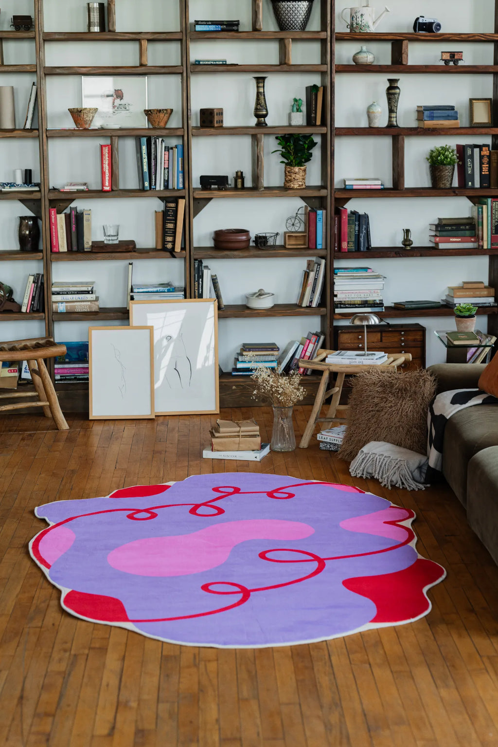 A lilac abstract rug with flowing red details spreads across the wood floor, creating a soft contrast with the bookshelves and cozy seating.
