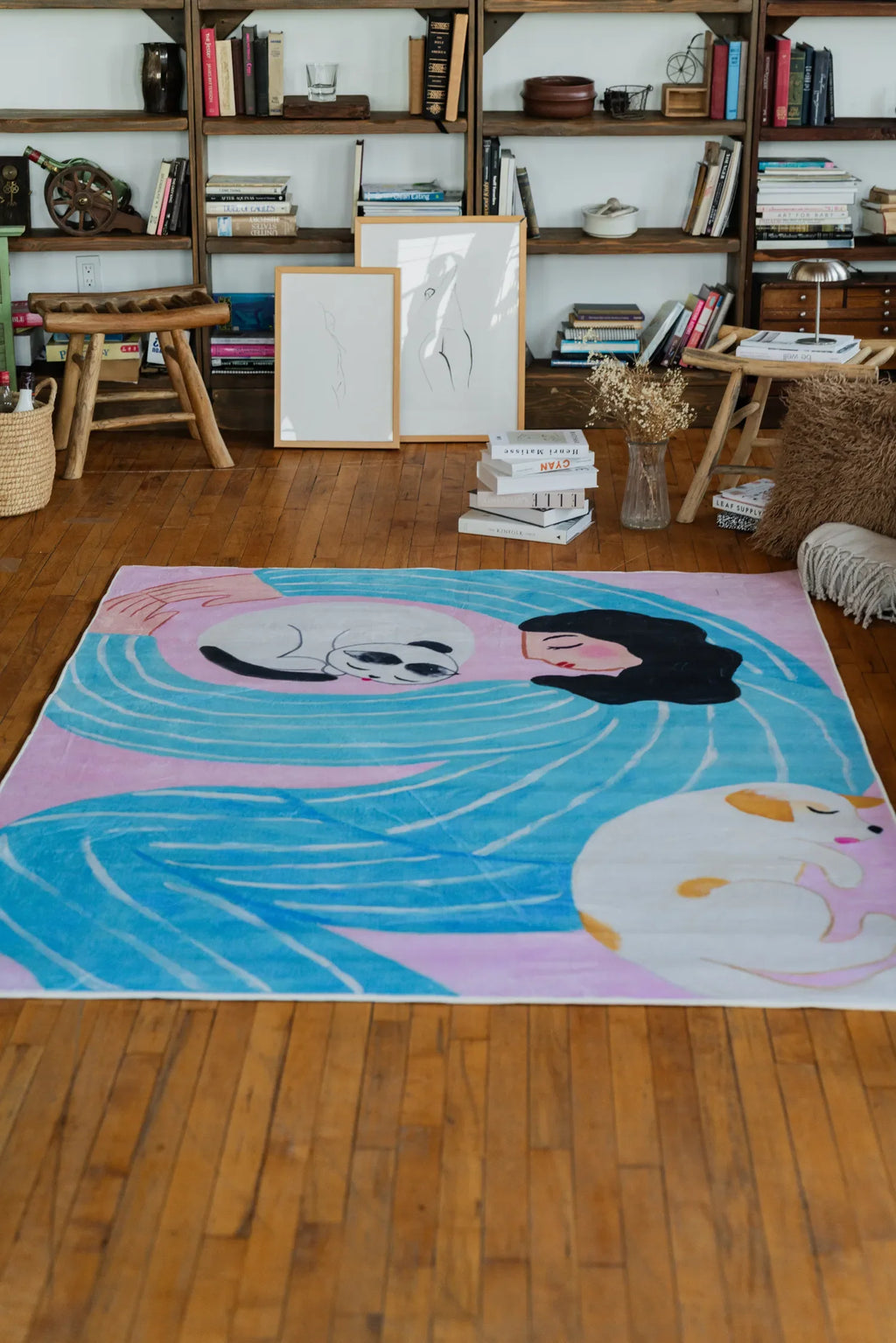 Funky Cat Lover Rug by Nimei in bold lilac and blue tones, styled on a wooden floor beside books and artwork in a cozy living space.