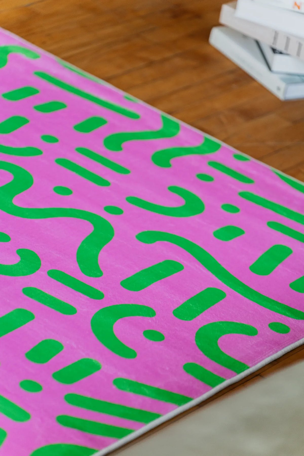 Graphic pink and green area rug with bold abstract lines styled beside stacked books on floor.