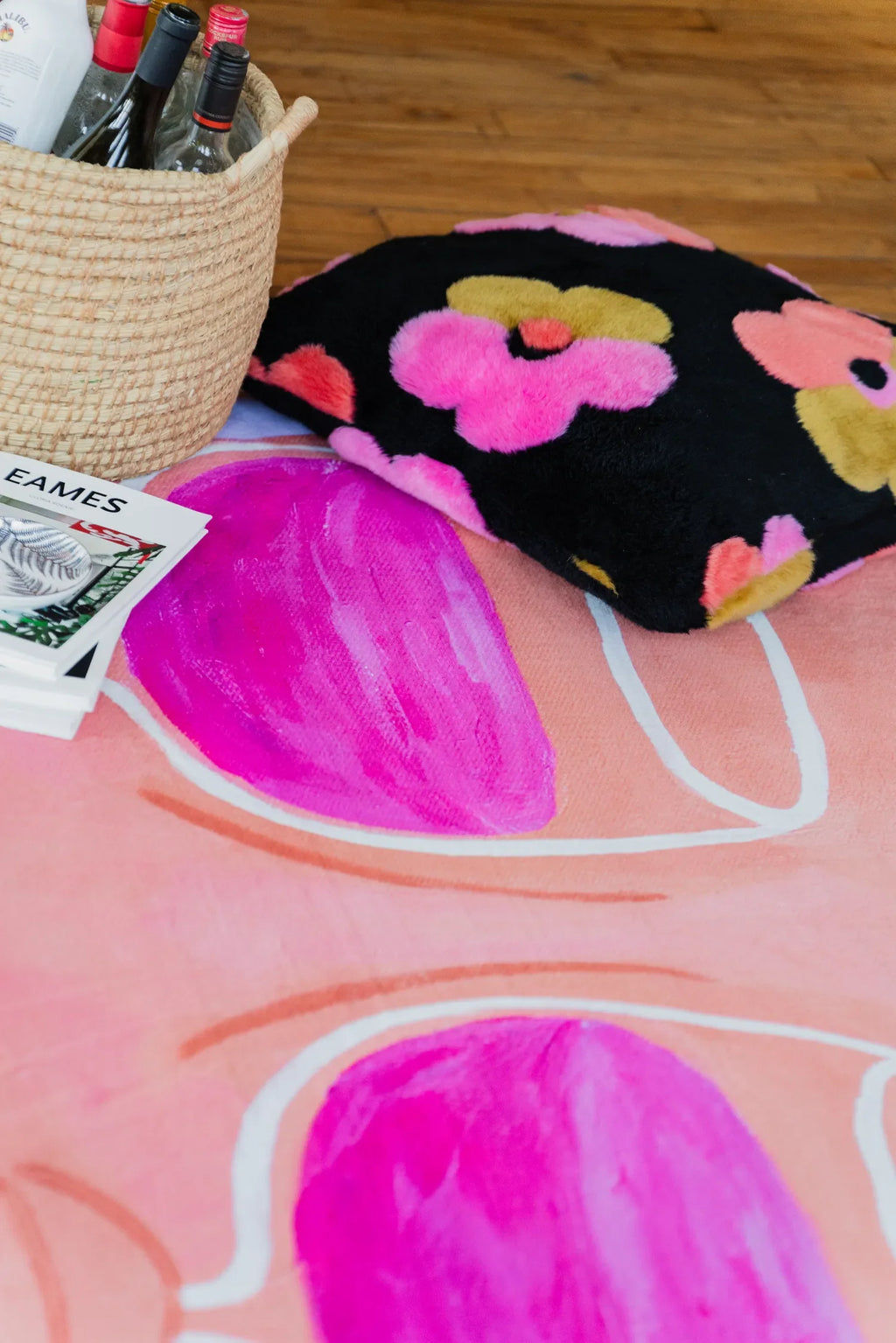 A funky art rug with vivid pink wine detail captured close to floral cushion and woven basket filled with bottles.