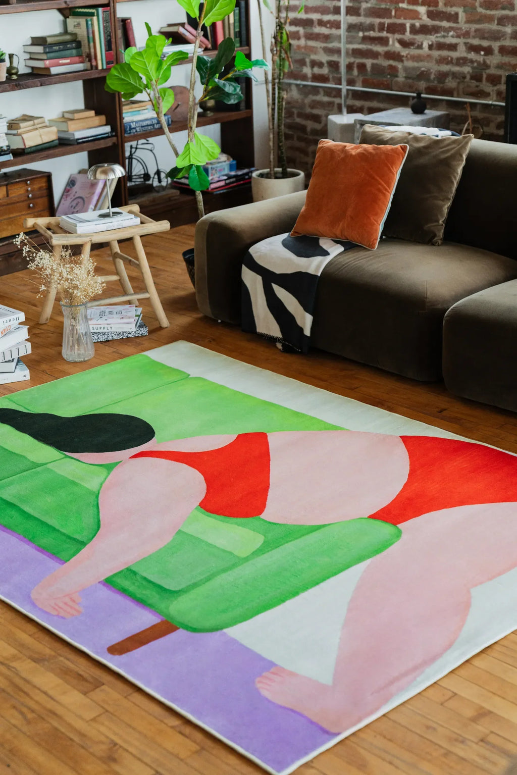 Modern Abstract Body Art Rug by Nimei in size 5'X7', placed beside a brown sofa with orange pillows and green plants in a loft-style room.