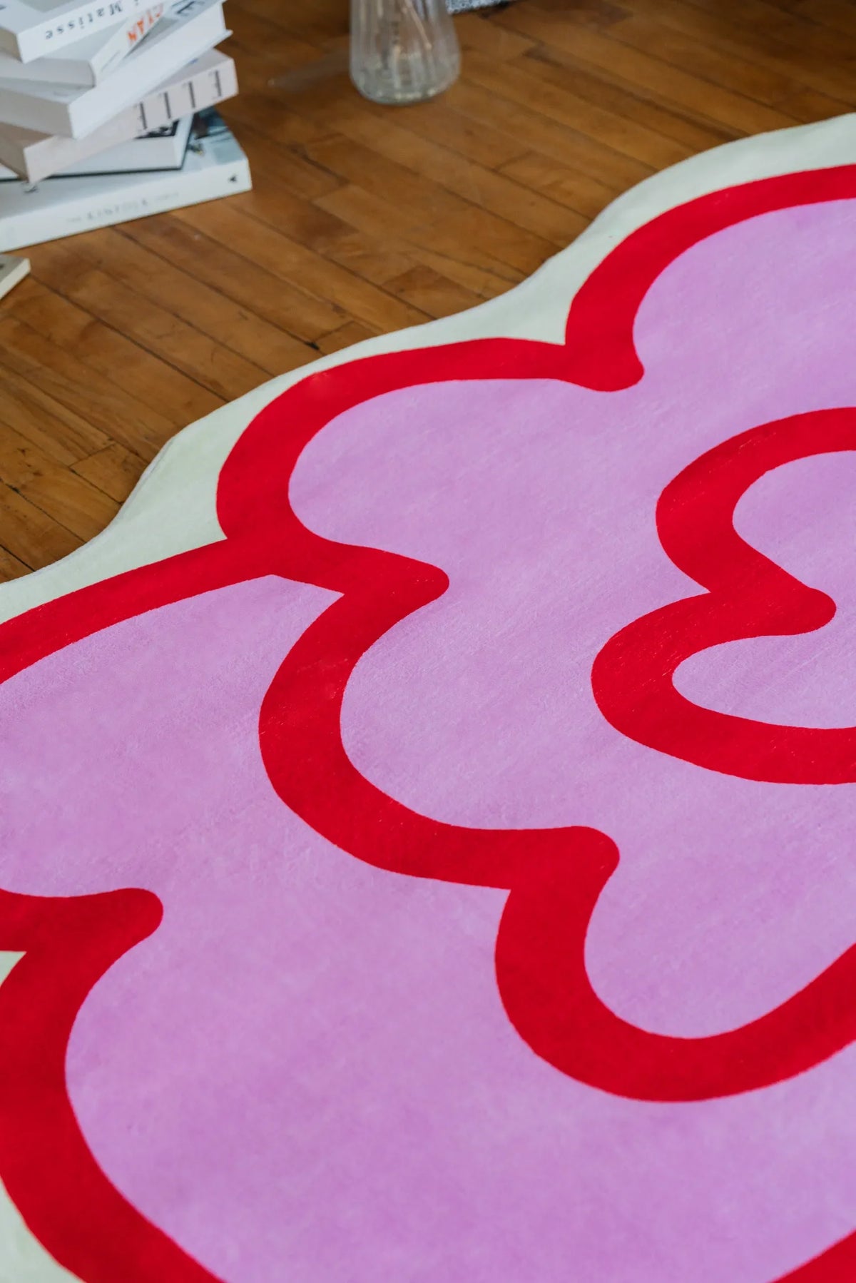 A pink funky flower shaped rug spreads across the wooden floor, creating a cheerful accent between the sofa and tall bookcase.