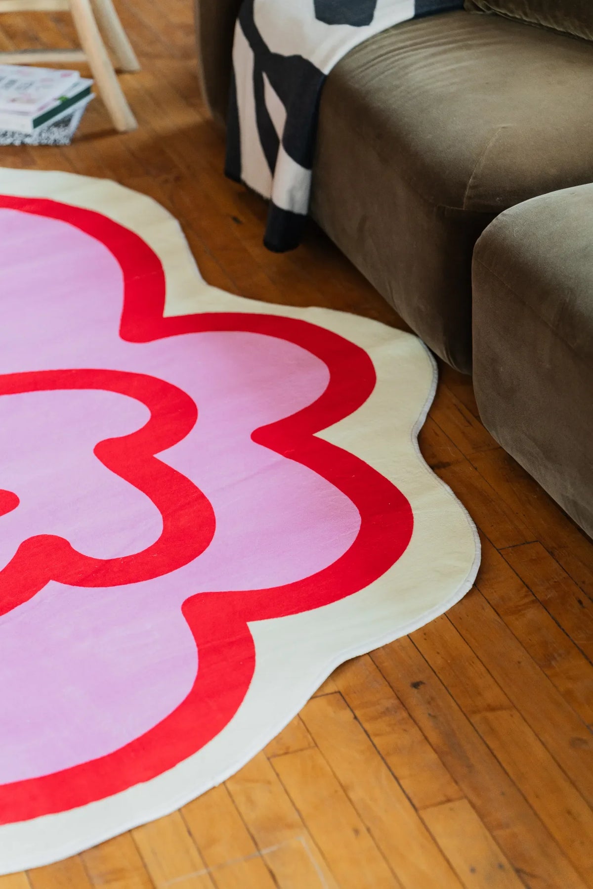 The pink funky flower shaped rug sits beside a sofa on wooden flooring, softening the living room corner with a cheerful vibe.
