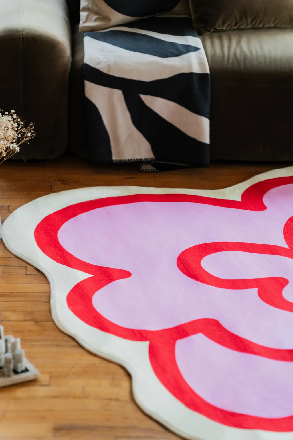 The pink funky flower shaped rug lies near a sofa on wood floor, adding a playful accent with its bold red outline.