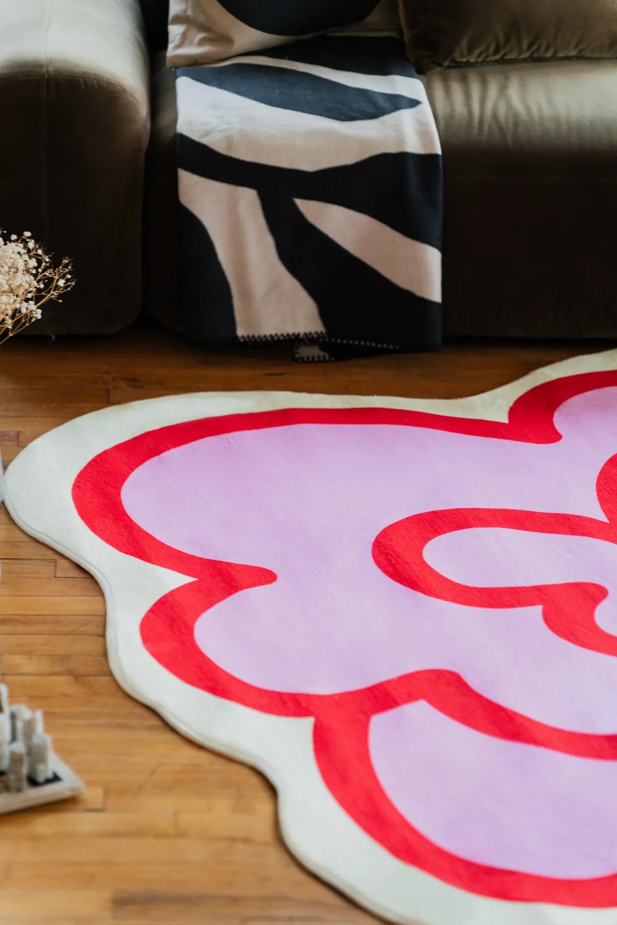 The pink funky flower shaped rug lies near a sofa on wood floor, adding a playful accent with its bold red outline.
