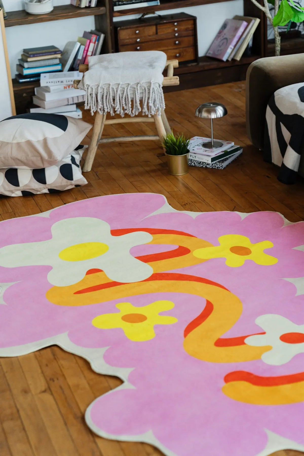 Modern area rug with irregular pink floral curves placed on wood floor near a cushioned chair and open shelving unit.