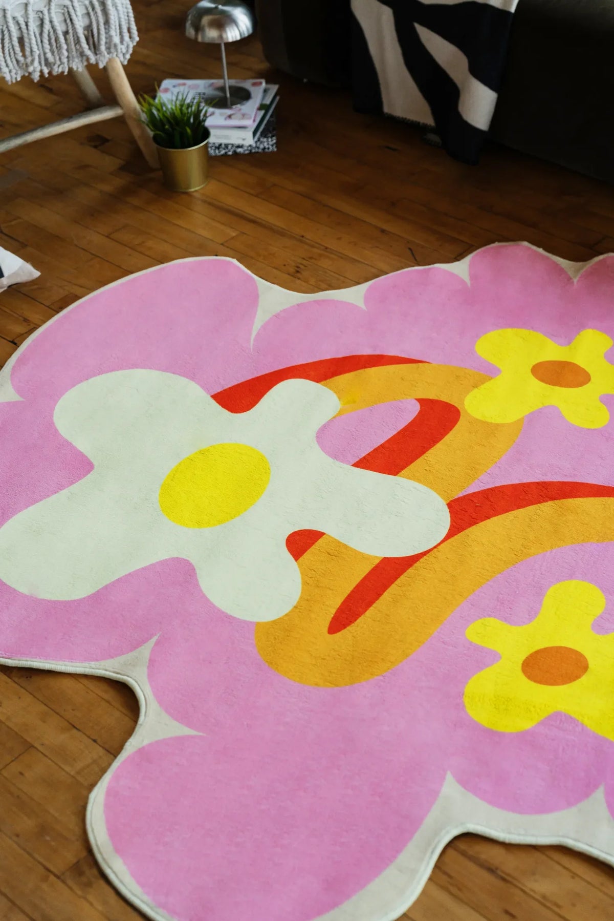 Irregular floral rug in pink and yellow tones laid on wood floor beside a dark sofa with patterned throw.