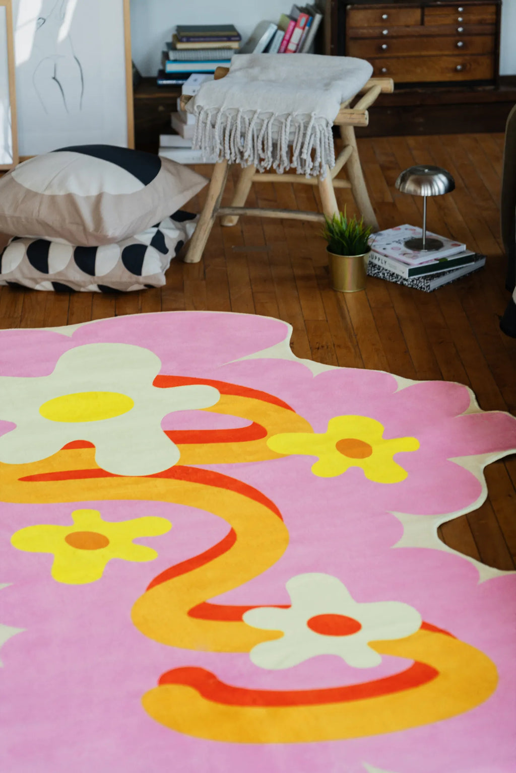 Modern area rug with wavy pink floral shapes spread on wood floor near a cushioned chair and open shelving.
