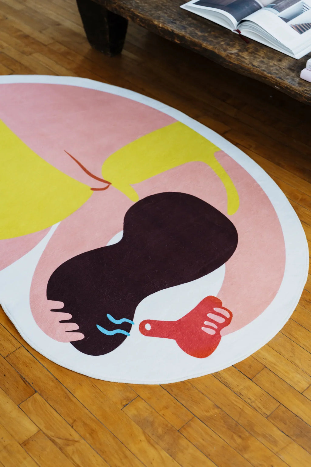 Close-up of the funky rug’s abstract figure, angled from bed corner showing vivid colors against hardwood floor.