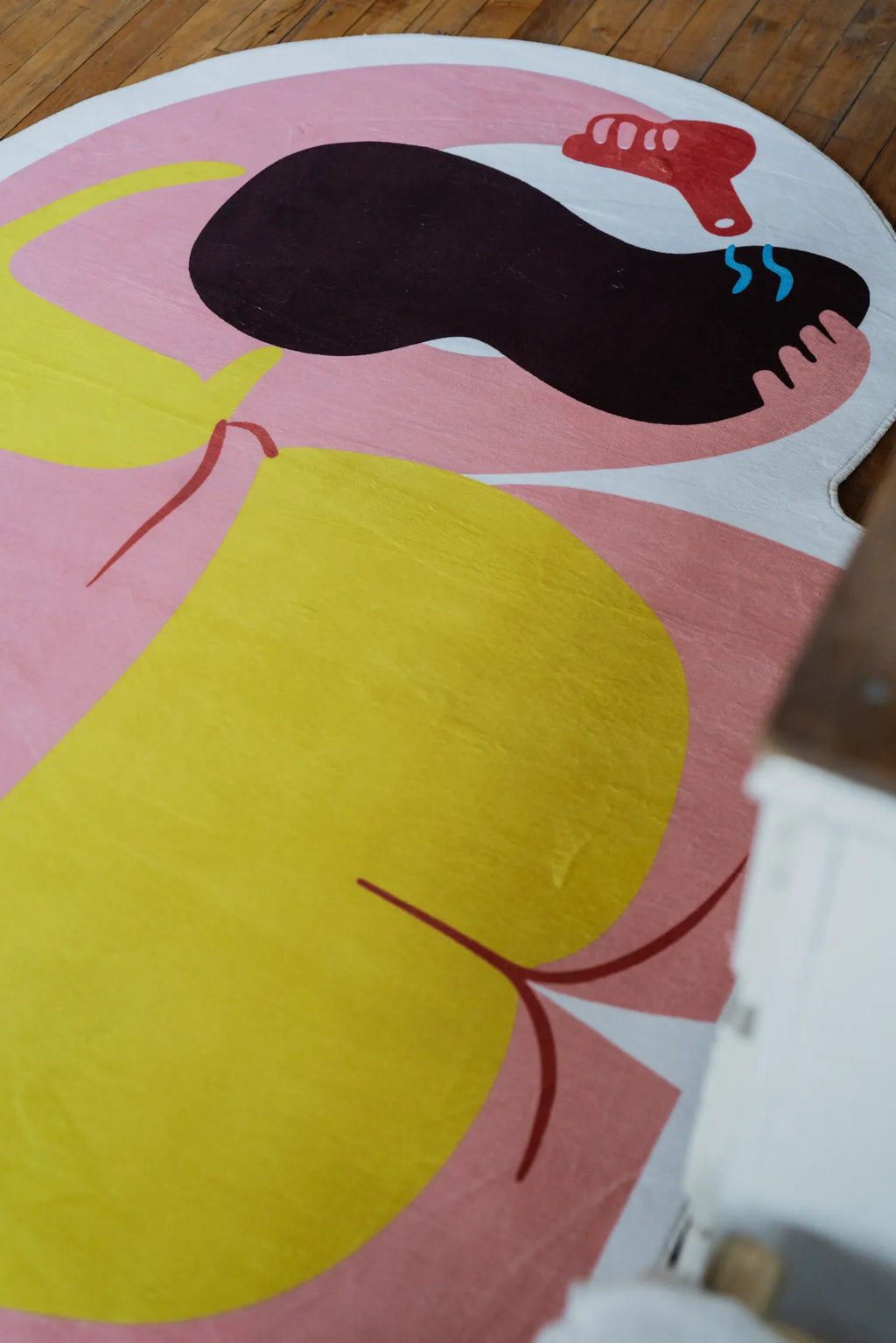 Close-up of funky body art rug from bedside angle, highlighting vivid yellow and pink blocks on hardwood floor.