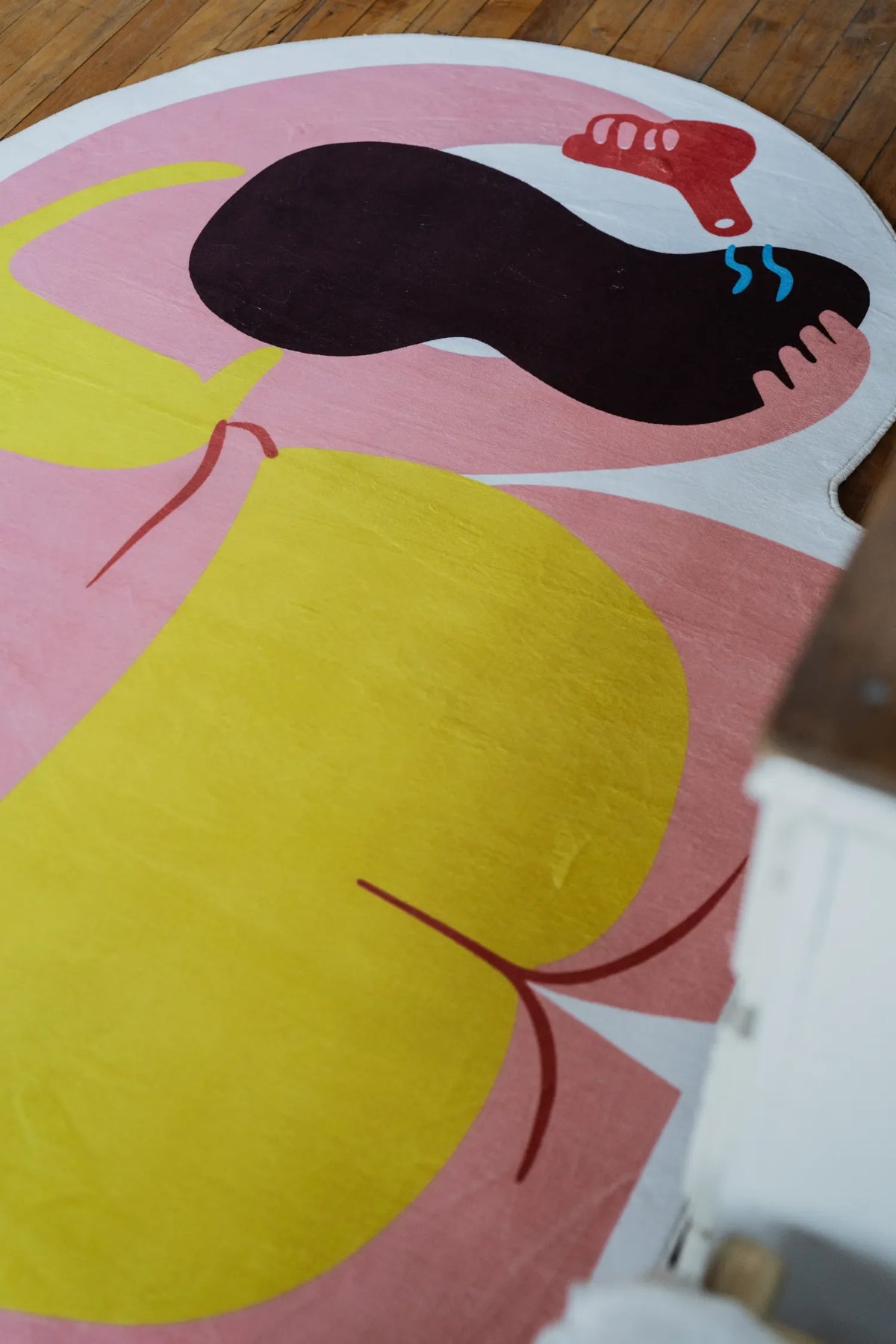 Close-up of funky body art rug from bedside angle, highlighting vivid yellow and pink blocks on hardwood floor.