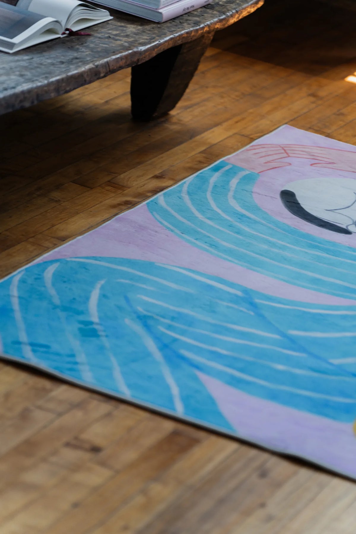 A corner view of the Funky Cat Lover Rug by Nimei in pink, blue, and lilac, styled next to an open book on a bench.