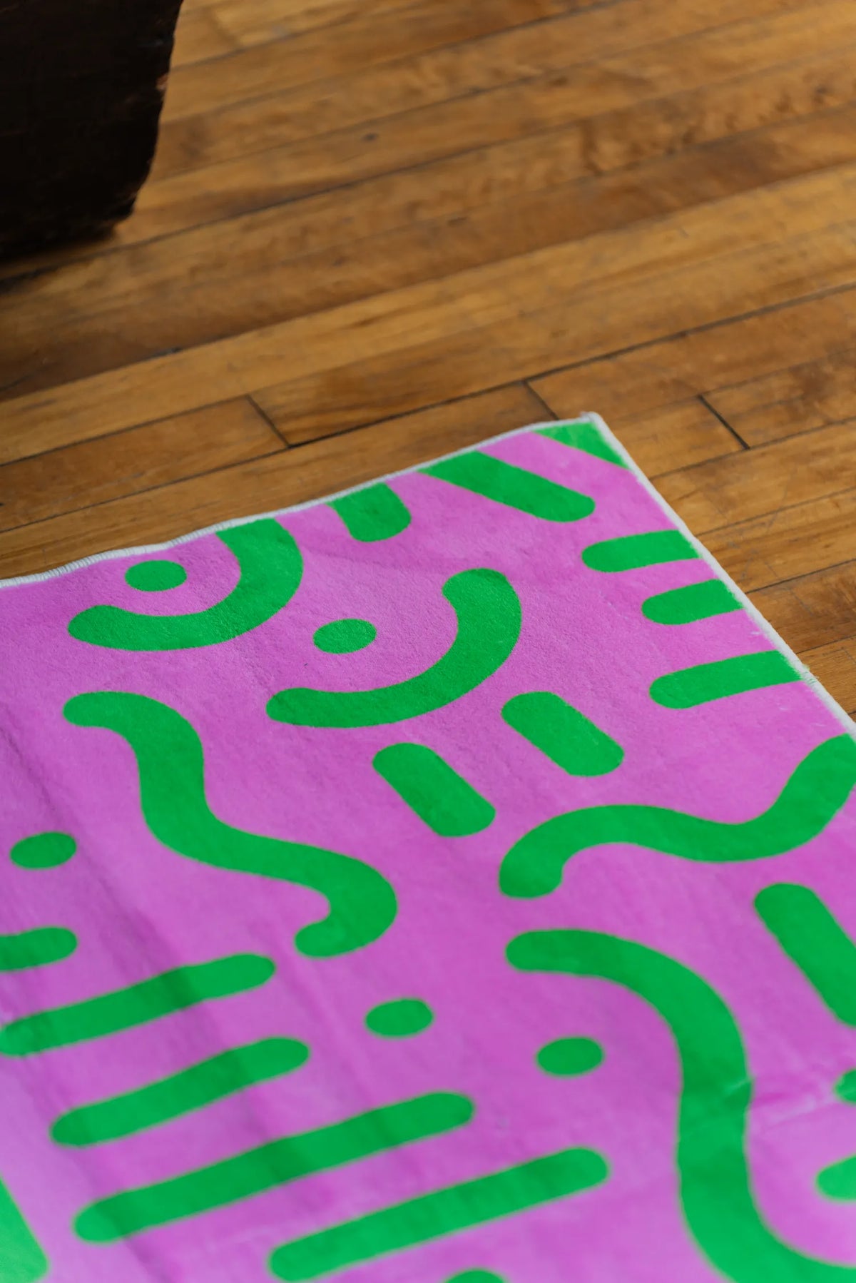 Close-up of retro pink and green patterned rug corner resting on polished wood floor beside dark sofa edge.