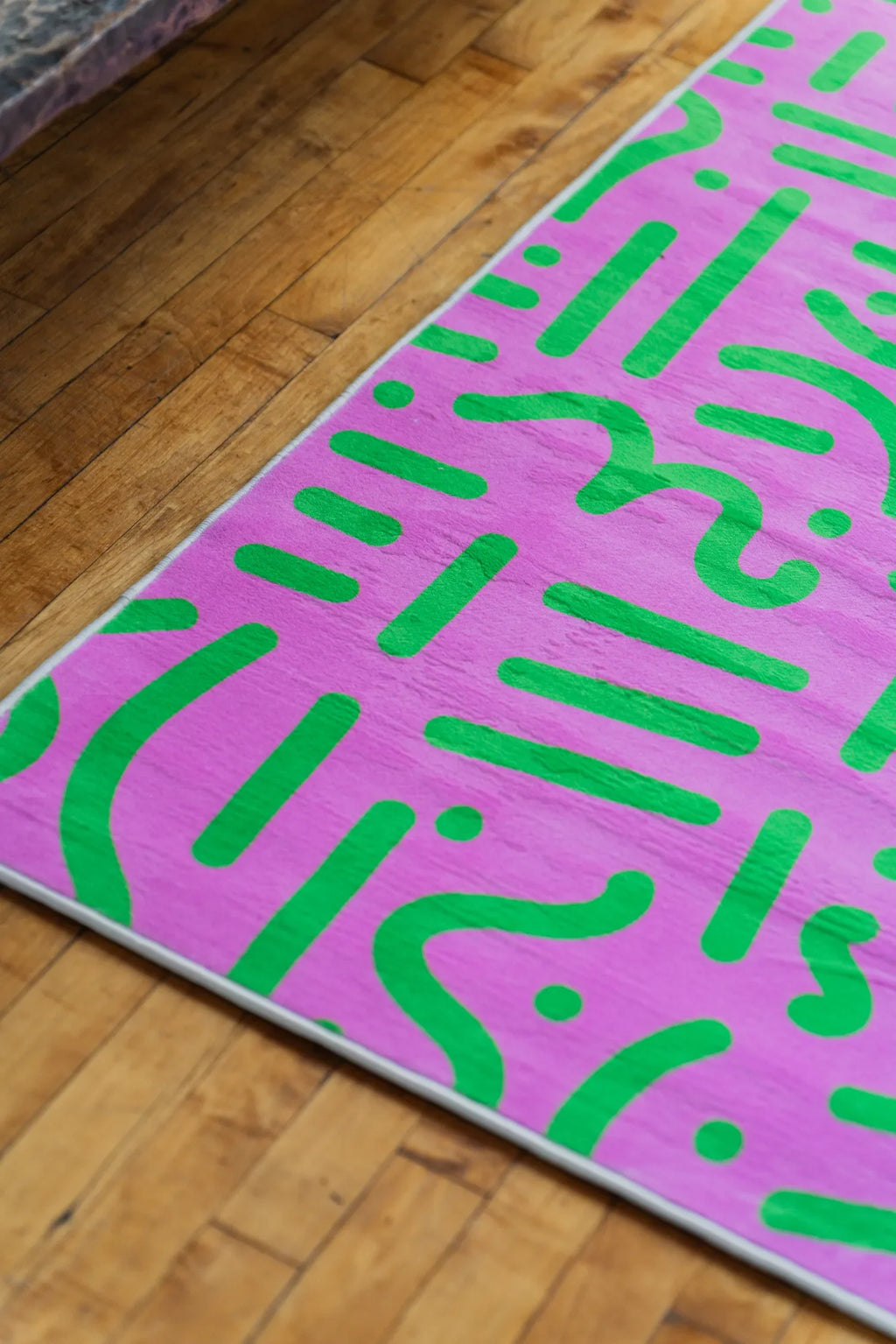 Retro graphic rug in pink and green detail view, highlighting curved lines against warm wood floor.