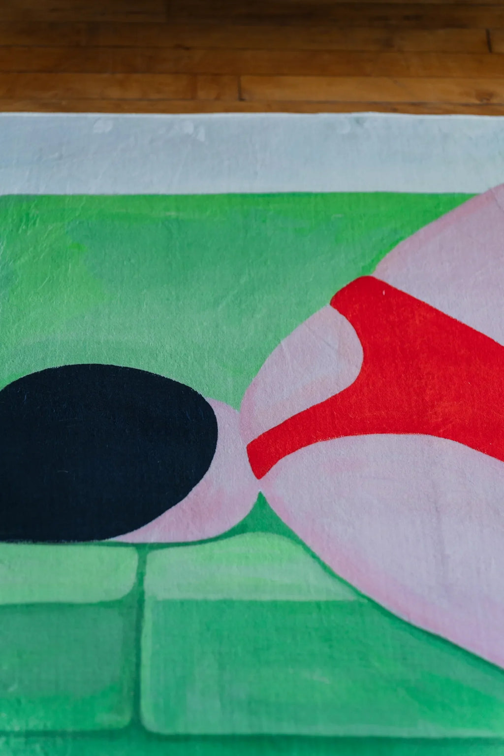 Close-up of the modern abstract body art rug highlighting bold red and green shapes against the wooden floor.
