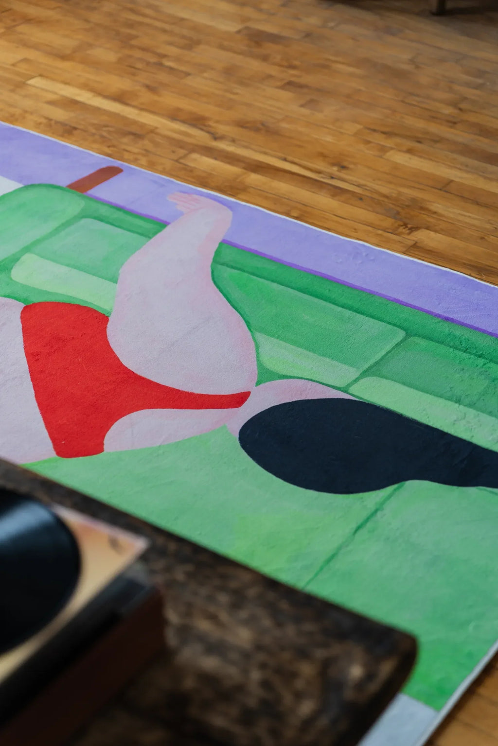 Vibrant abstract body art rug featuring reclining figure design, partially shown near a rustic wooden table.