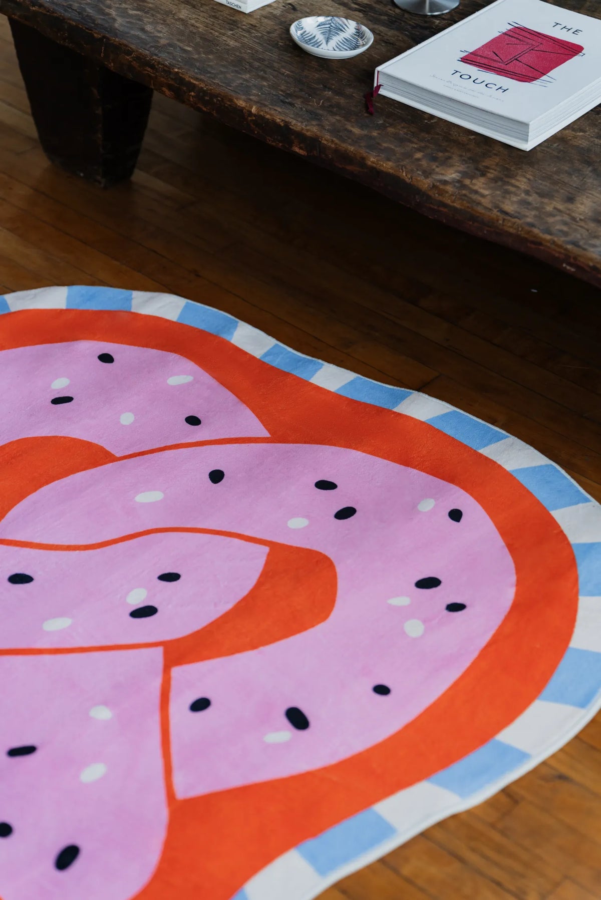 Pink and Orange Pretzel-Shaped Cute Rug by Megan Roy placed beside a rustic wooden table