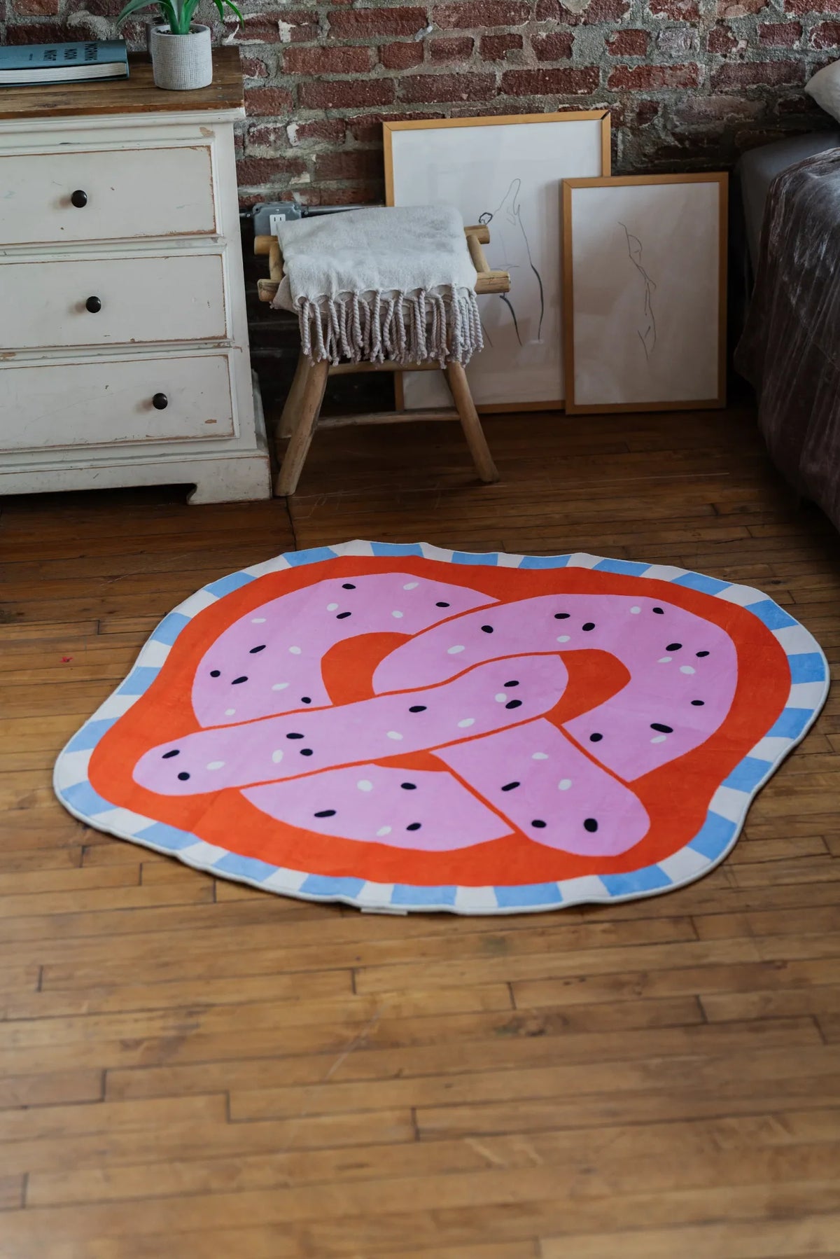 A playful pink pretzel-shaped rug adding color on wood floor near framed artwork