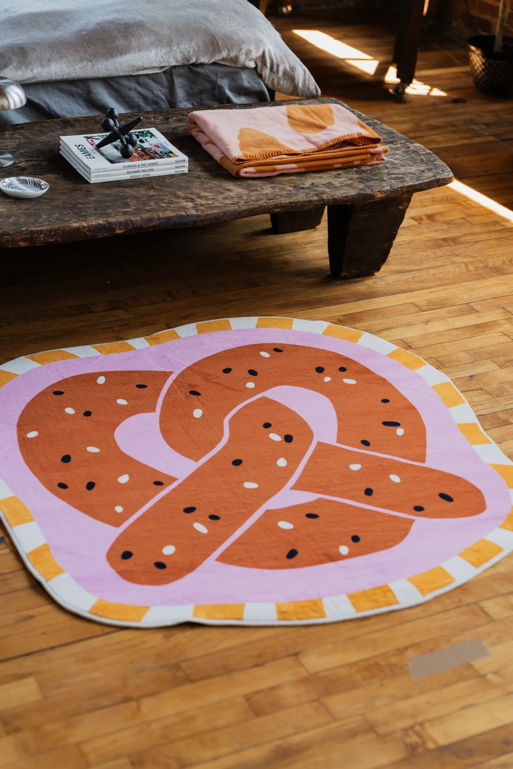 Brown pretzel-shaped rug resting by a low table with folded blankets on wood floor