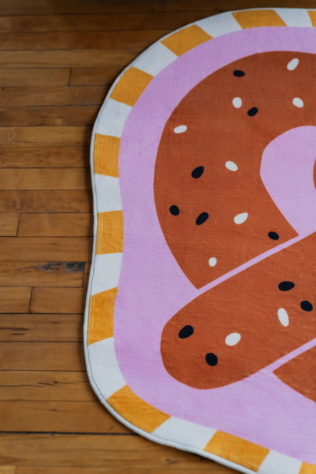 Brown pretzel-shaped rug with playful sprinkles detail resting on a wooden floor