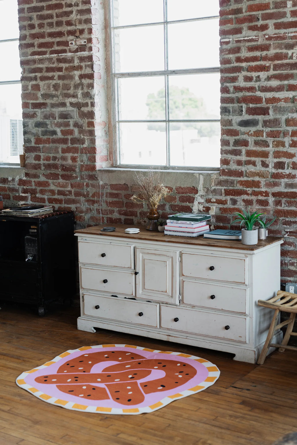 Brown pretzel-shaped rug by Megan Roy set near a white dresser against a brick wall