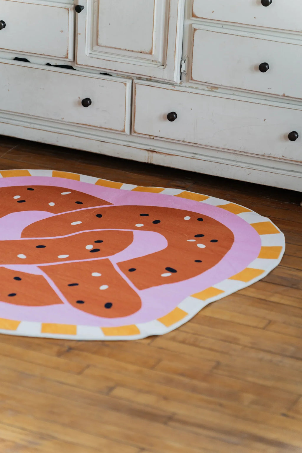 Brown pretzel-shaped rug adding a cozy touch on wood floor in front of vintage dresser