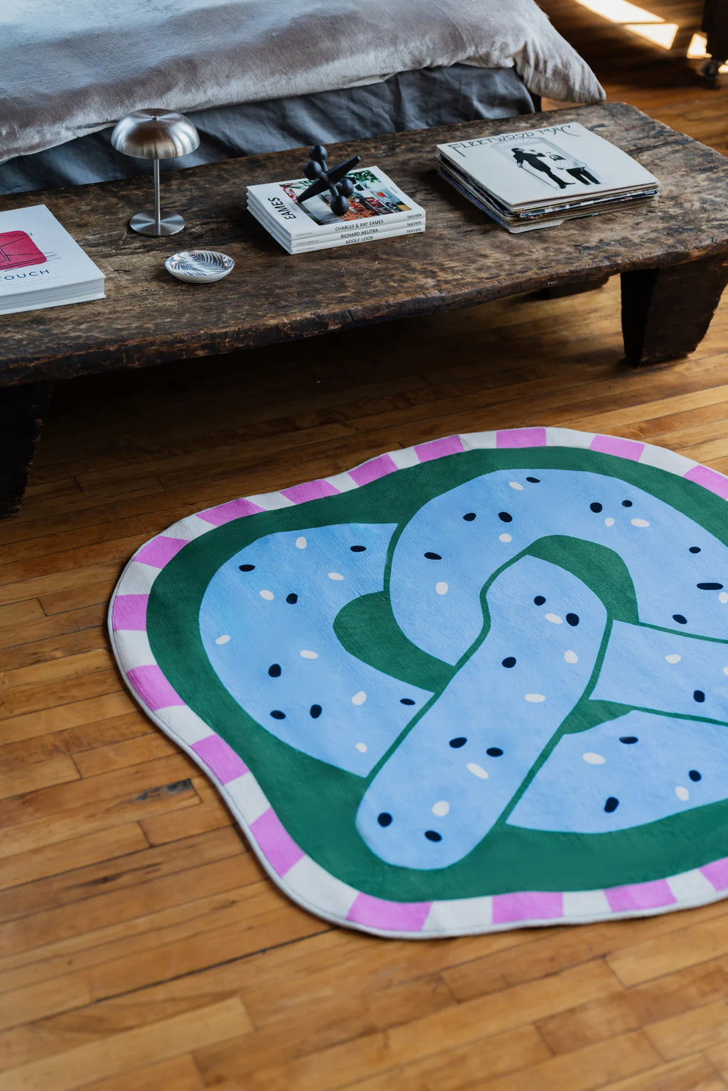Blue pretzel rug placed near a wooden bench at the foot of the bed adding playful detail to the bedroom decor.