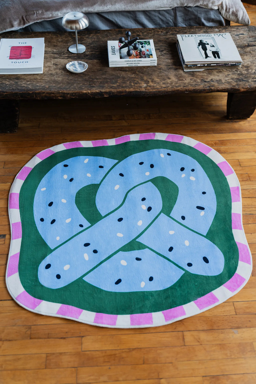Blue pretzel rug placed near a wooden bench in bedroom interior with books and decor