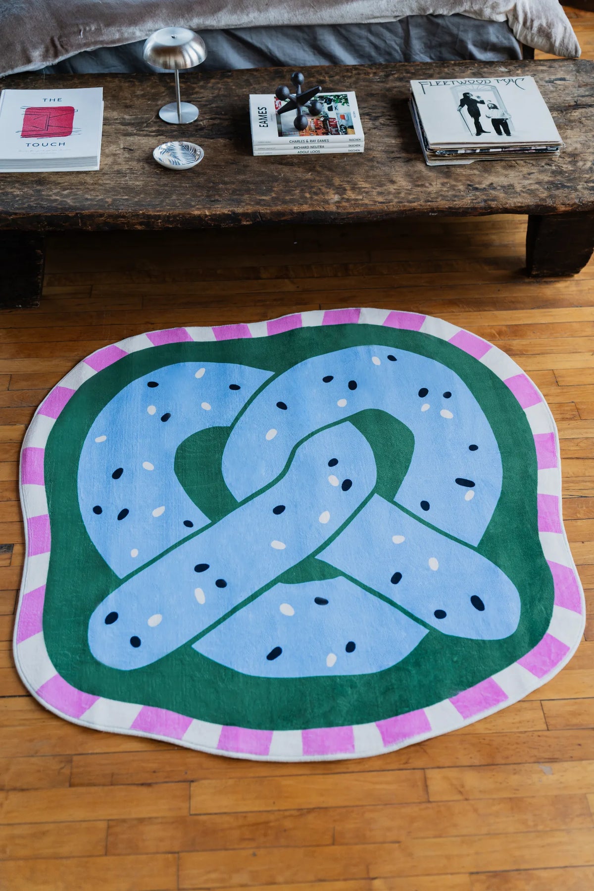 Blue pretzel rug placed near a wooden bench in bedroom interior with books and decor