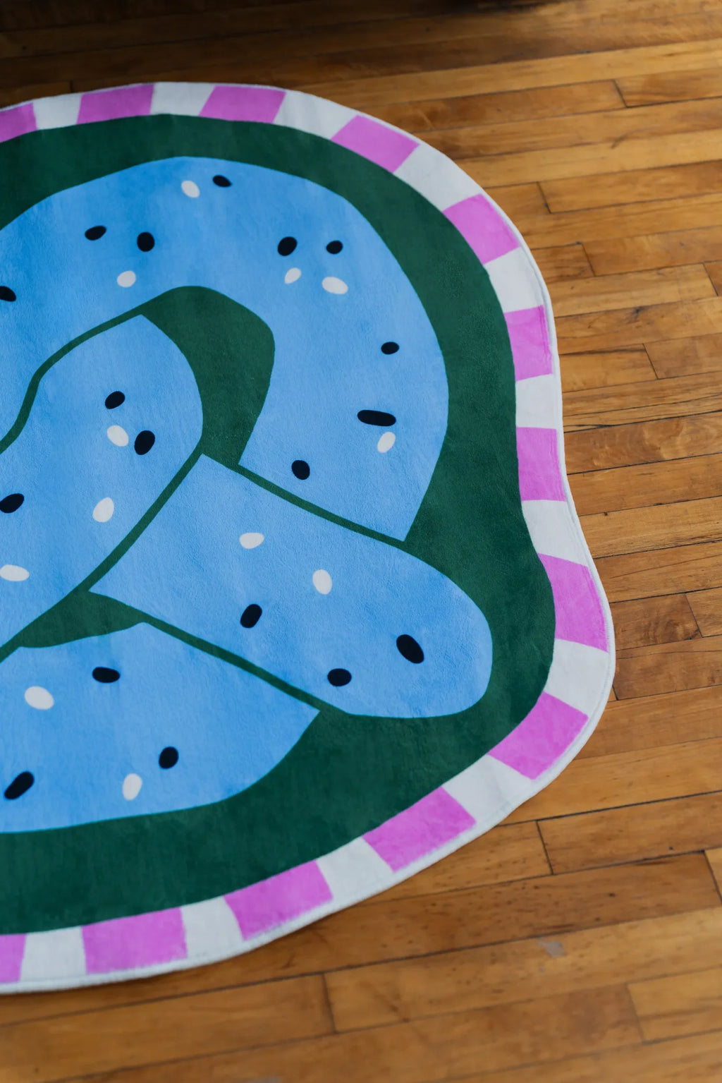 Close up of blue pretzel rug showing playful knot design and colorful border on wood floor