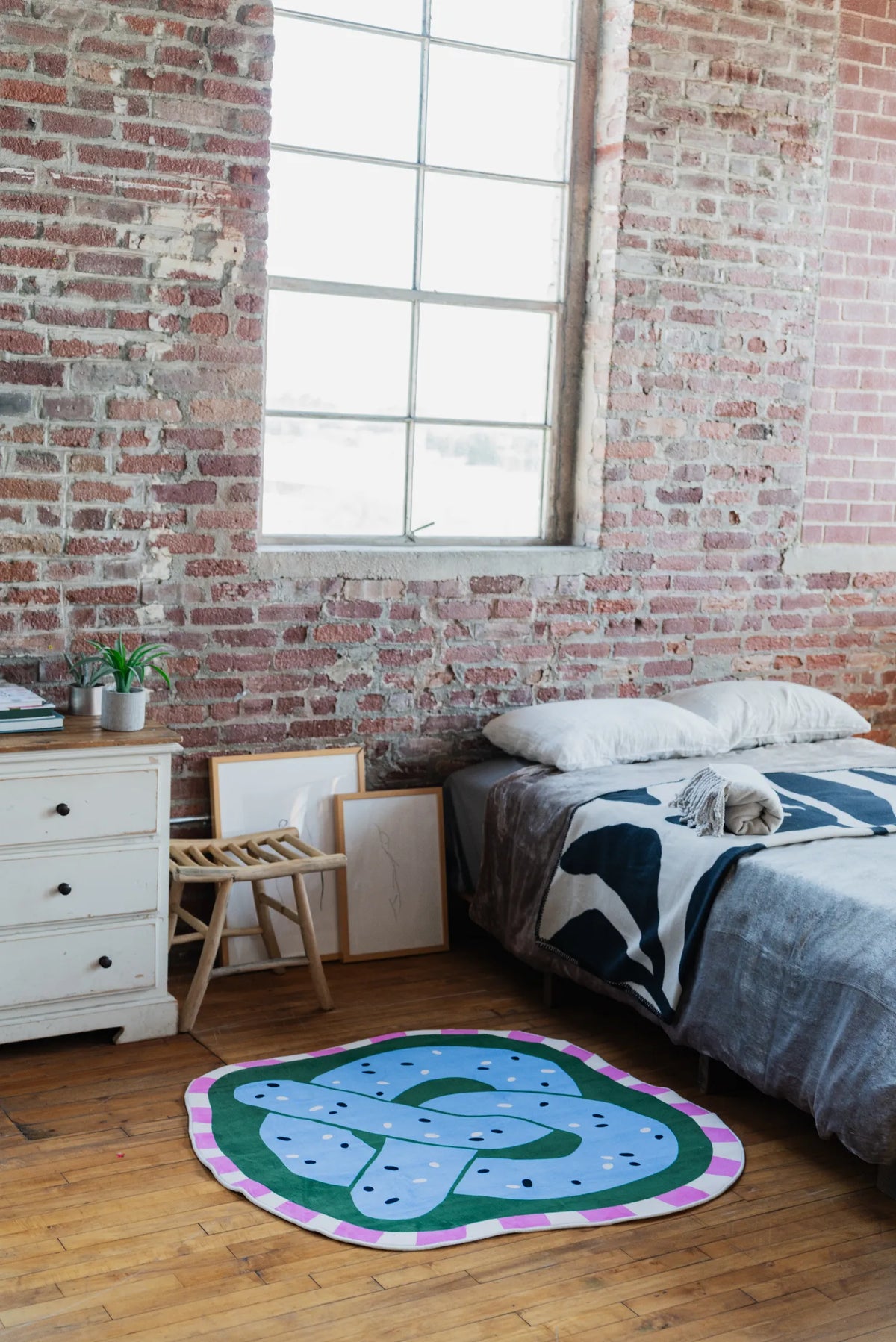 Pretzel-Shaped Cute Rug by Megan Roy in blue styled in an industrial bedroom with brick wall and wooden floor