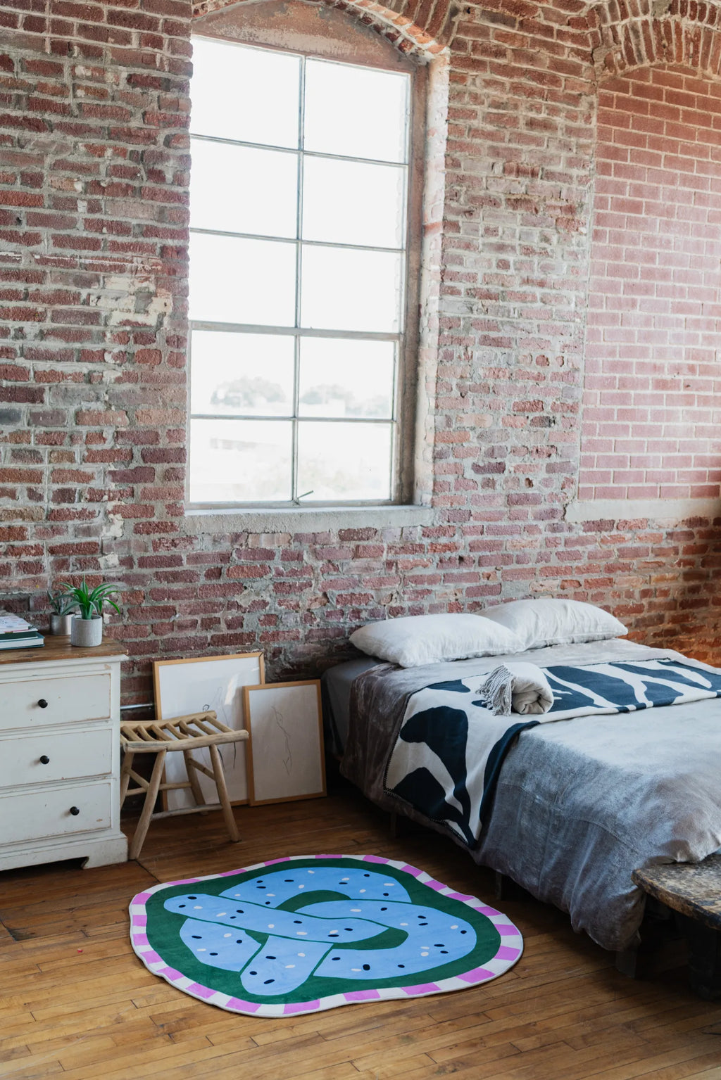 Pretzel-Shaped Cute Rug in blue styled beside a bed with brick walls and natural light