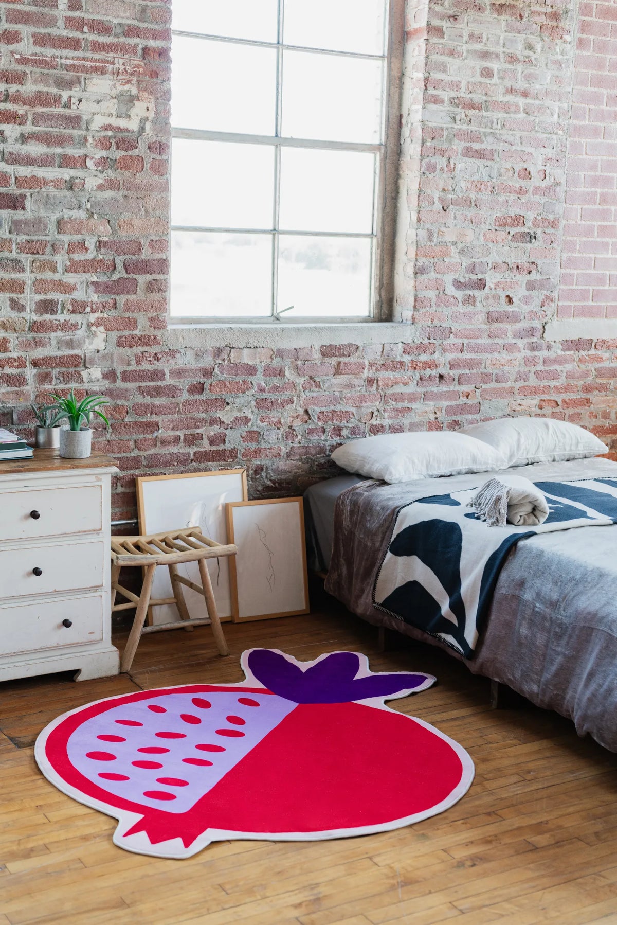 Red Pomegranate Shaped Irregular Rug placed in a modern loft bedroom with brick wall, styled beside a low bed and white nightstand.