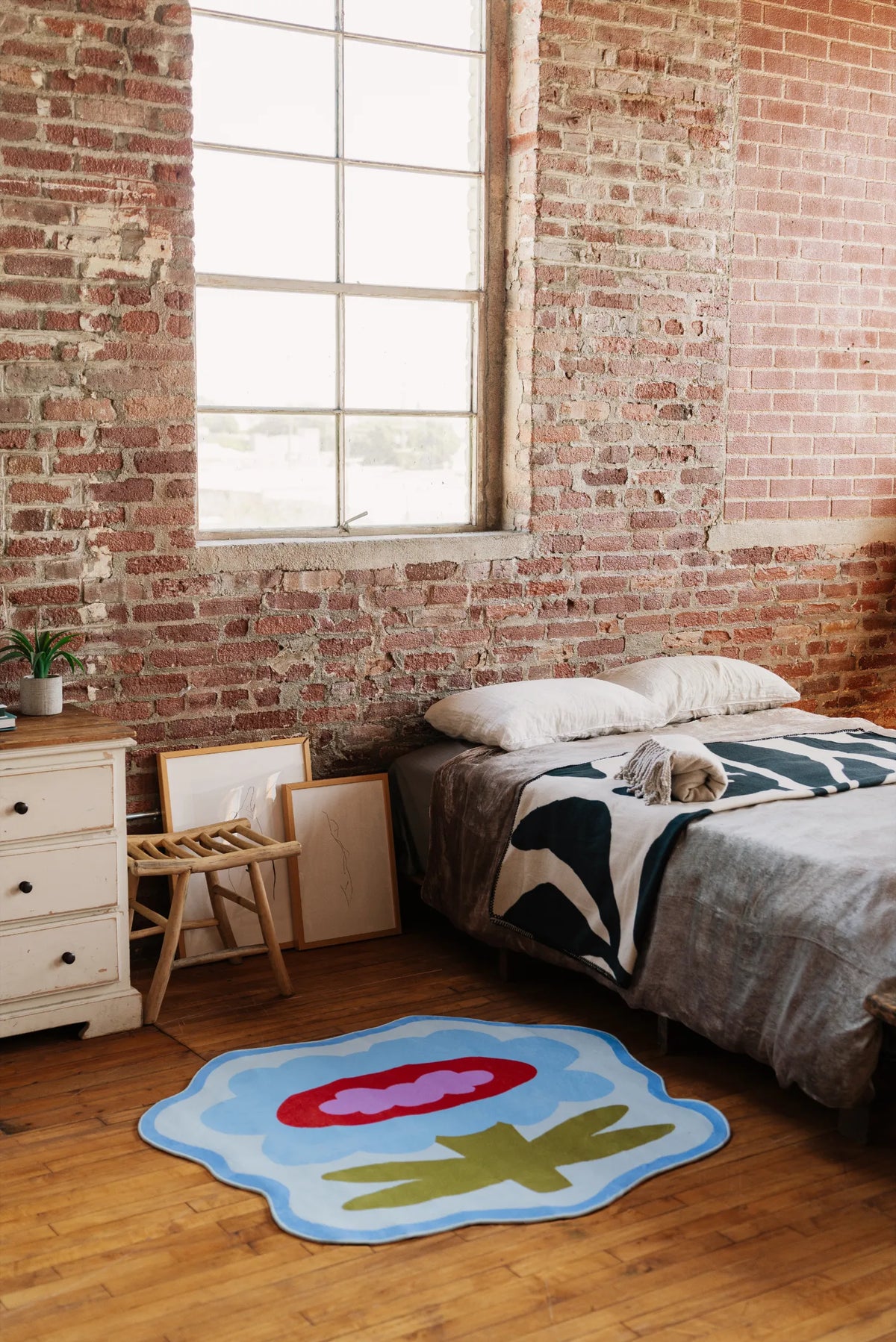 Blue flower rug styled beside low bed and rustic nightstand, adding playful rug accent on wood floor.